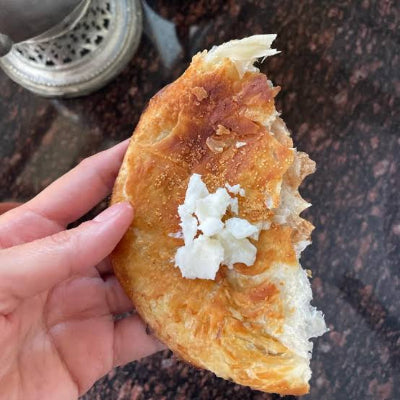 Hand holding a pastry with cheese filling on a textured surface